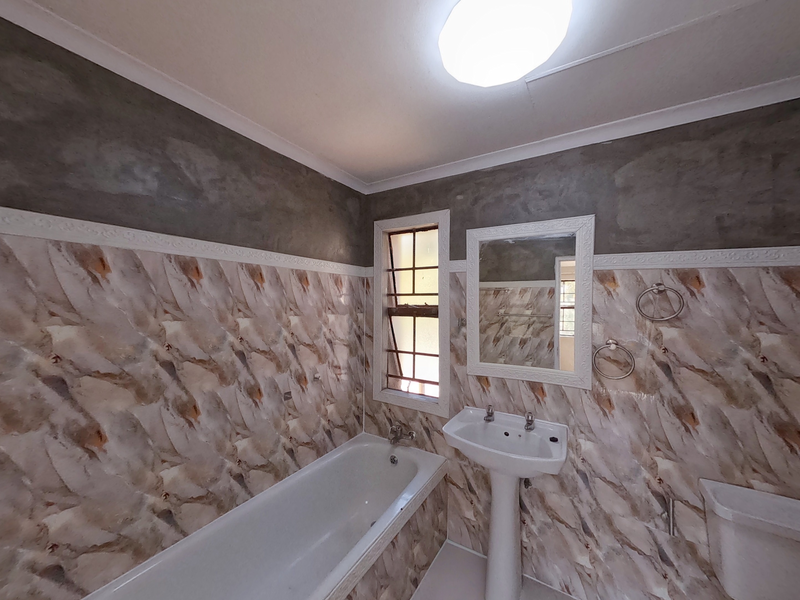 A bathroom featuring a bathtub, pedestal sink, and mirror, with partially finished wall surfaces and dated tiling throughout.