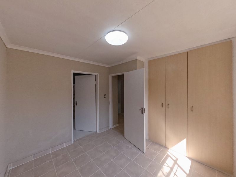 A bright, empty bedroom featuring neutral tiled flooring and built-in wooden cupboards, offering a clean and versatile space ready for personalization.