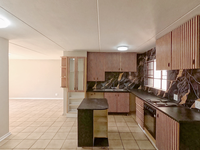 Open-plan kitchen area featuring dated cabinetry, built-in oven and hob, and tiled flooring, flowing into an adjacent living space.