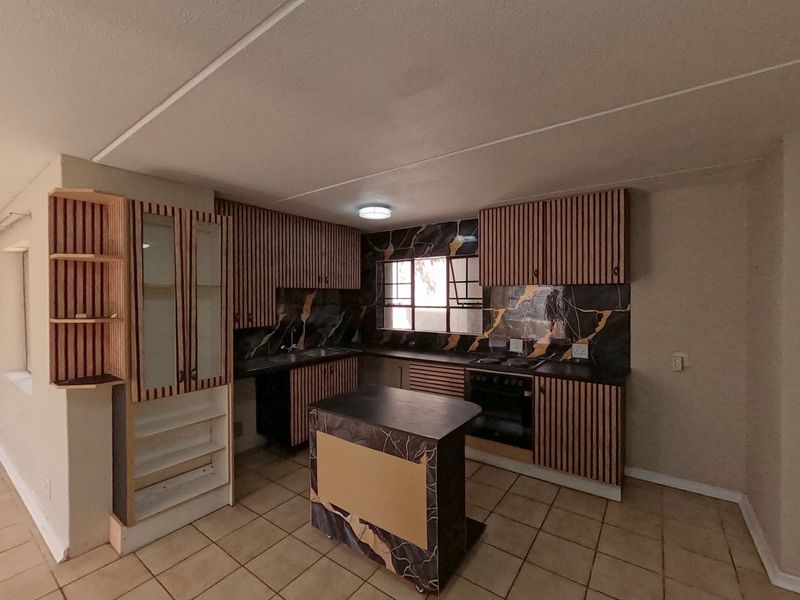 A functional kitchen featuring built-in cabinetry, a marble-effect splashback, integrated oven, hob, and a central island, offering a practical layout for culinary activities.