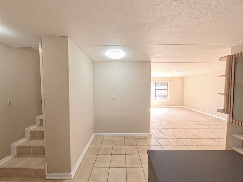Spacious open-plan living area featuring tiled flooring, a staircase, and built-in cabinetry, offering a versatile layout for dining and lounge arrangements.