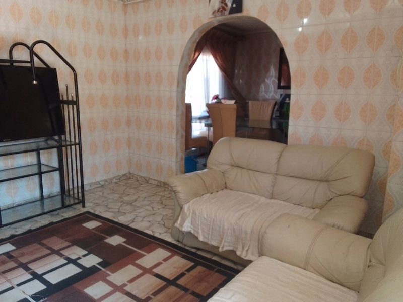 Living room featuring an arched doorway leading to an adjacent space, with dated wall and floor tiling throughout.