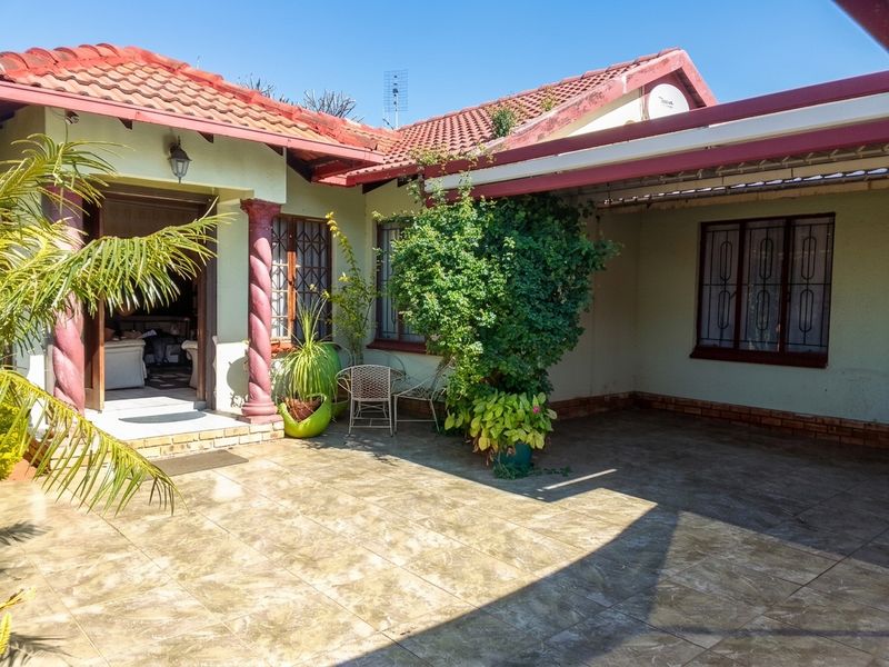 A covered patio area featuring tiled flooring, decorative columns, and security bars on the windows, providing a functional outdoor space.