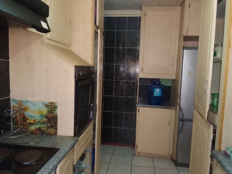 A compact kitchen featuring built-in cabinetry, a fitted oven and hob, and tiled finishes. The space offers a functional layout ready for modernization.