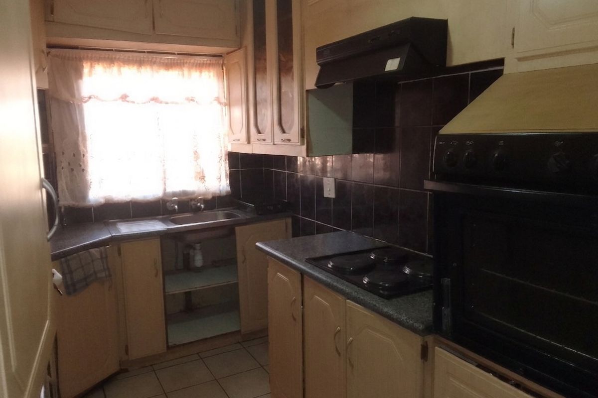 A dated kitchen featuring built-in cabinetry, a stainless steel sink, electric hob, and oven with a tiled backsplash and flooring.