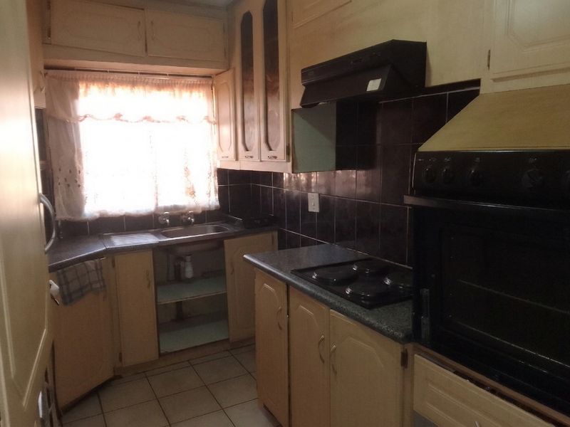A dated kitchen featuring built-in cabinetry, a stainless steel sink, electric hob, and oven with a tiled backsplash and flooring.