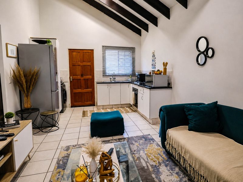 Open-plan living area featuring a kitchen with built-in cabinetry, tiled floors, and striking exposed timber ceiling beams, creating a bright and functional space.