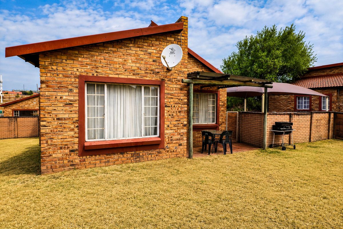 Rear view of a face brick townhouse featuring a paved patio area with a timber pergola and a private garden space.