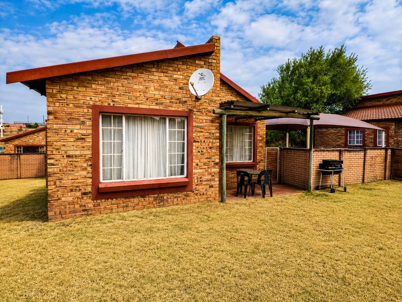 Rear view of a face brick townhouse featuring a paved patio area with a timber pergola and a private garden space.