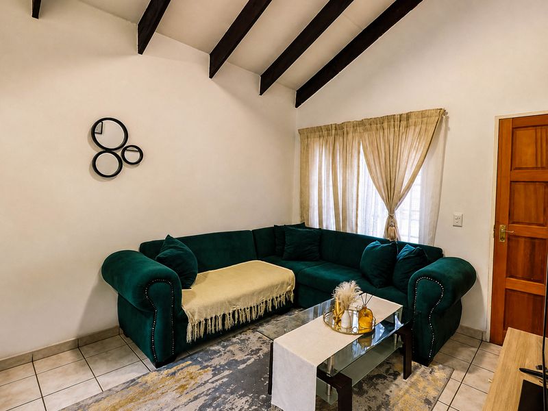 A cozy living room featuring exposed timber ceiling beams, neutral tiled flooring, and a classic timber door, creating a warm and inviting atmosphere.