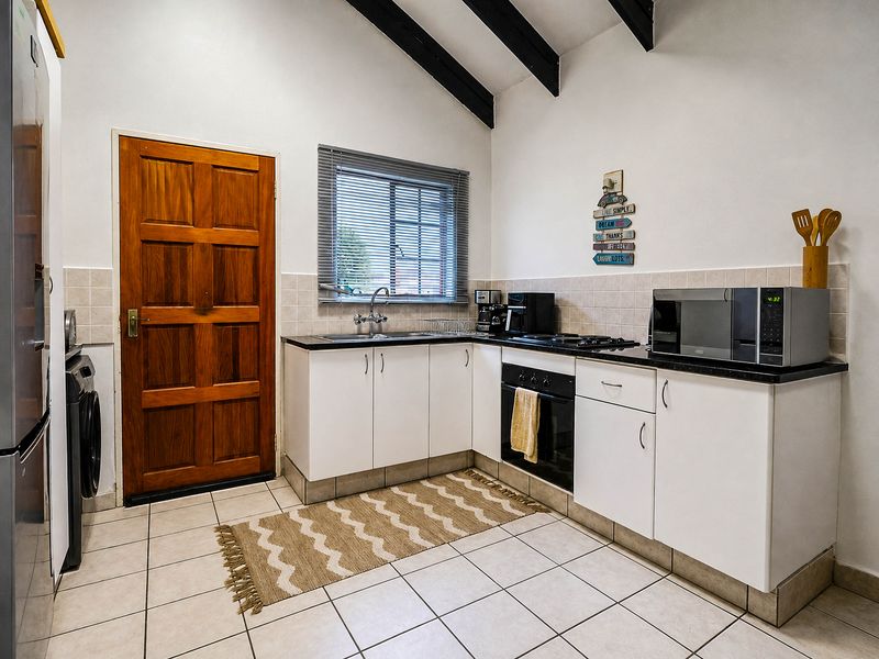 A functional kitchen featuring white cabinetry, dark countertops, tiled flooring, and exposed ceiling beams, providing a practical workspace with integrated oven and hob.