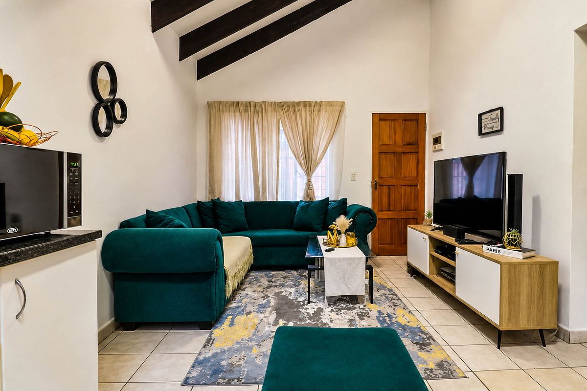 A bright living room featuring a high vaulted ceiling with exposed timber beams, tiled flooring, and a solid timber door.