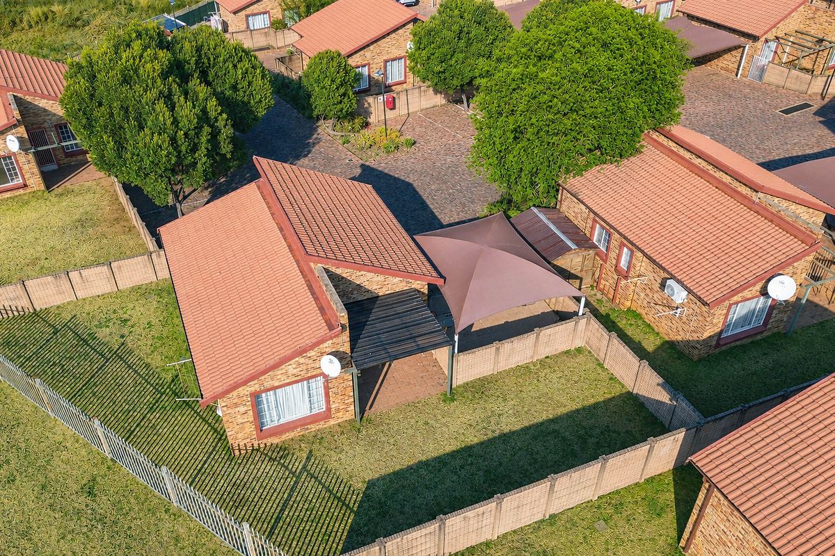 Aerial view of a townhouse complex featuring brick units with tiled roofs, paved driveways, and private fenced garden areas with shade sails.