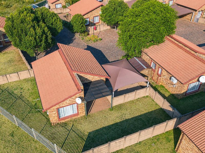 Aerial view of a townhouse complex featuring brick units with tiled roofs, paved driveways, and private fenced garden areas with shade sails.