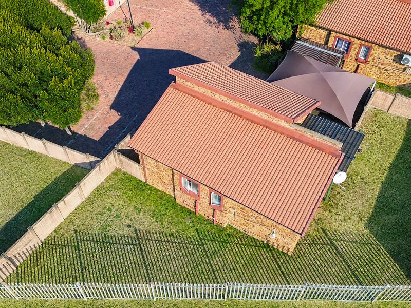 Aerial view of a townhouse property featuring a tiled roof, facebrick facade, private garden, and secure perimeter fencing.