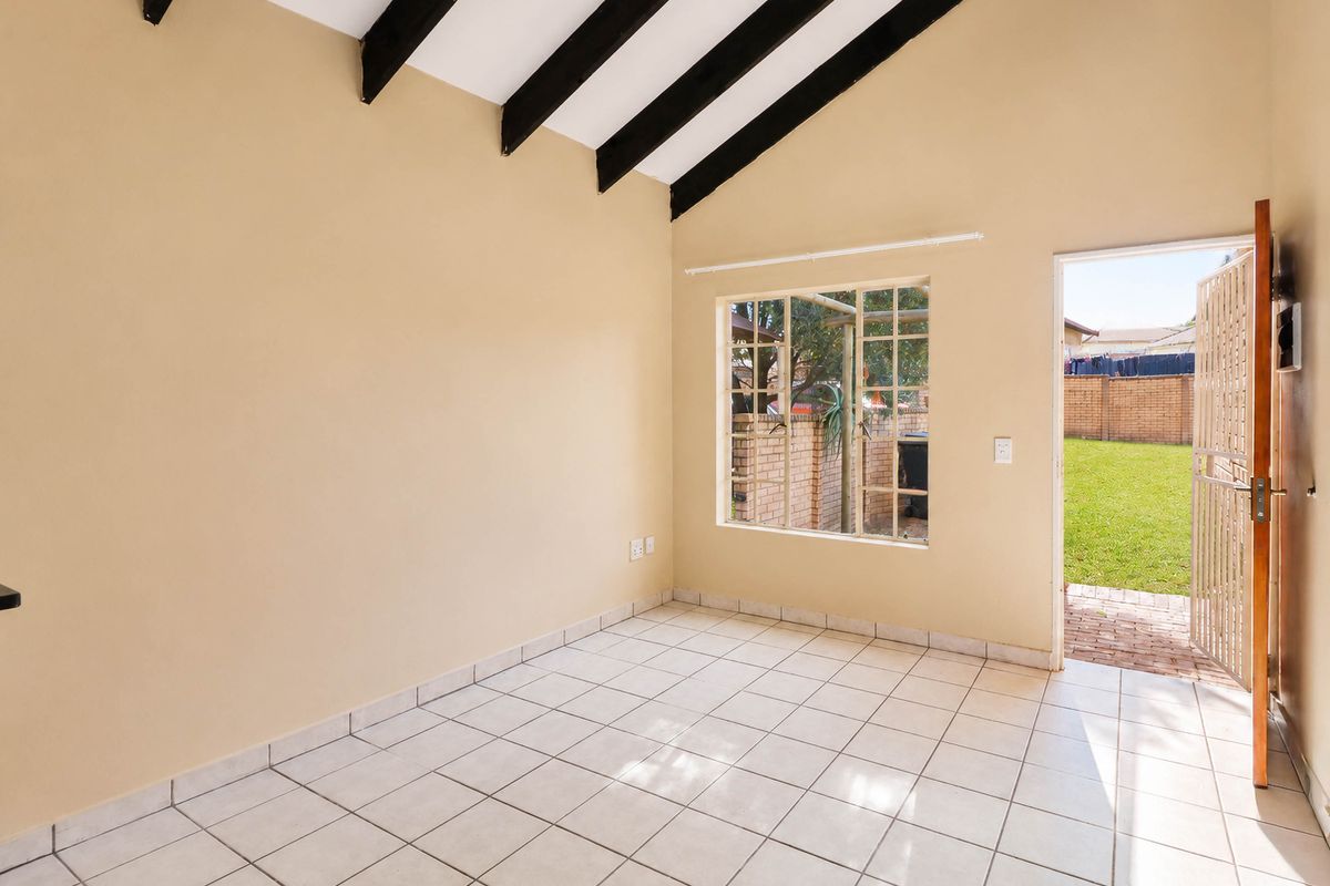 Bright, empty living area featuring vaulted ceilings with exposed timber beams, tiled flooring, and direct access to the rear garden through a security gate.