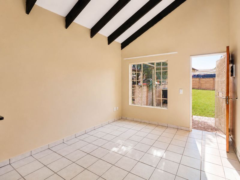 Bright, empty living area featuring vaulted ceilings with exposed timber beams, tiled flooring, and direct access to the rear garden through a security gate.
