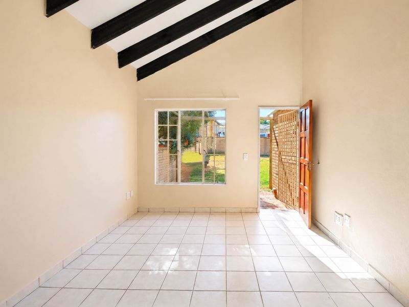 An empty living area featuring high vaulted ceilings with exposed timber beams, tiled flooring, and direct access to the rear garden.