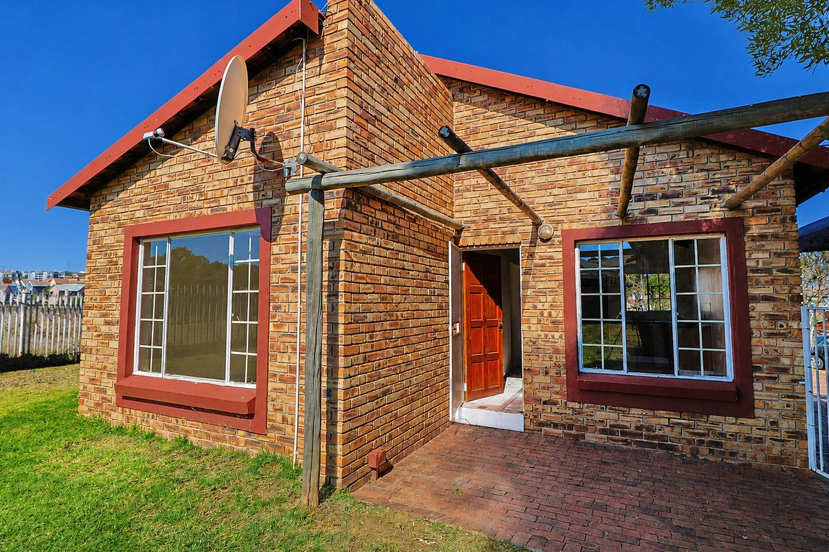 Rear exterior view of a face brick townhouse featuring a paved patio area and a timber pergola structure.