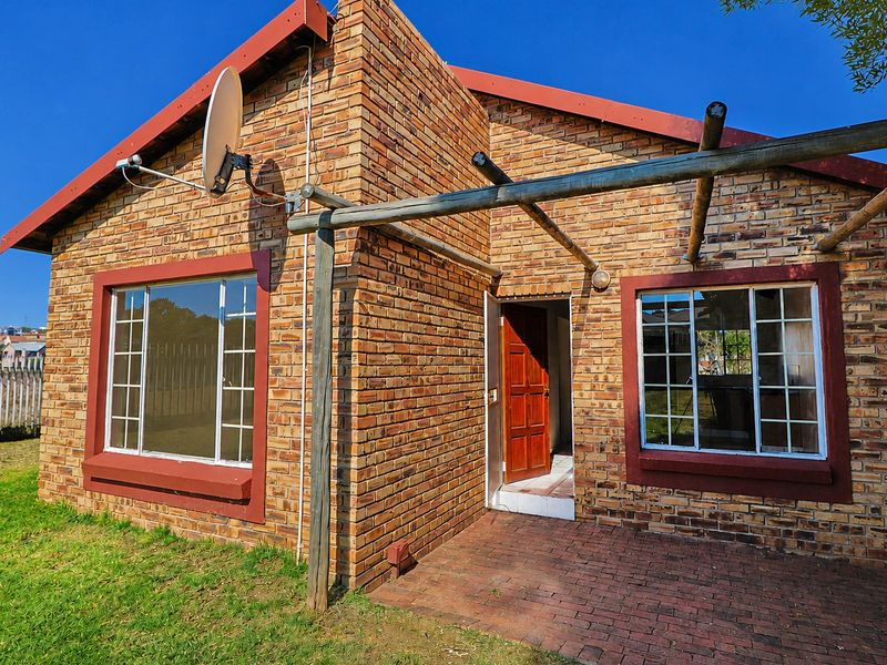 Rear exterior view of a face brick townhouse featuring a paved patio area and a timber pergola structure.