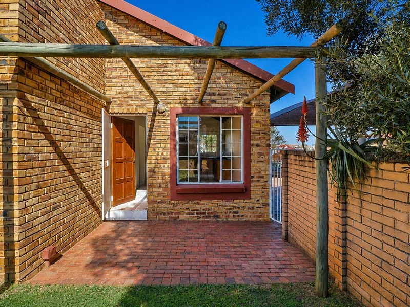 A rear exterior view of the townhouse featuring a brick facade, a timber pergola over a paved patio, and a secure entrance door.
