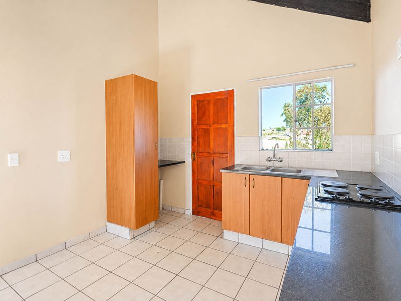 A functional kitchen featuring granite countertops, built-in cabinetry, a double sink, and an electric hob, with tiled flooring and a high vaulted ceiling.