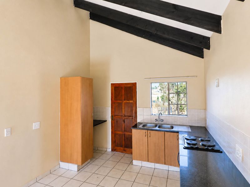 A functional kitchen featuring exposed timber beams, black granite countertops, a built-in electric hob, and tiled flooring in an open-plan layout.