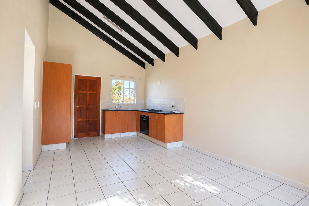 An empty kitchen featuring exposed timber ceiling beams, tiled flooring, built-in cabinetry, and a built-in oven and hob.
