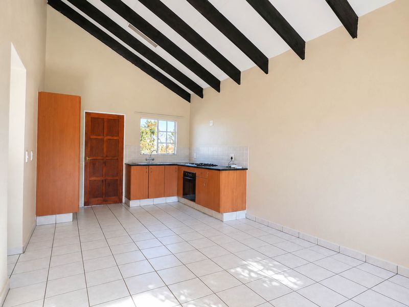 An empty kitchen featuring exposed timber ceiling beams, tiled flooring, built-in cabinetry, and a built-in oven and hob.