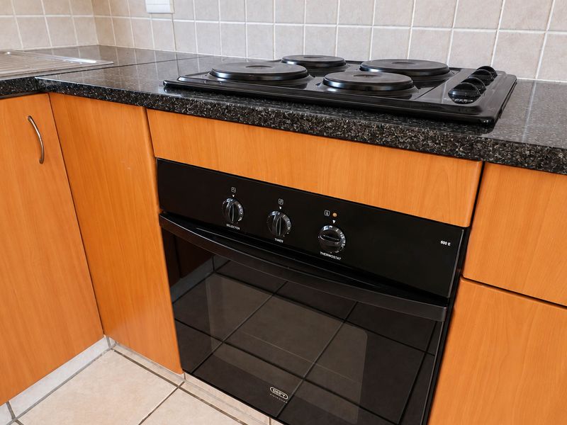 A functional kitchen area featuring a built-in oven, electric hob, granite countertops, and light wood-finish cabinetry with a tiled backsplash.