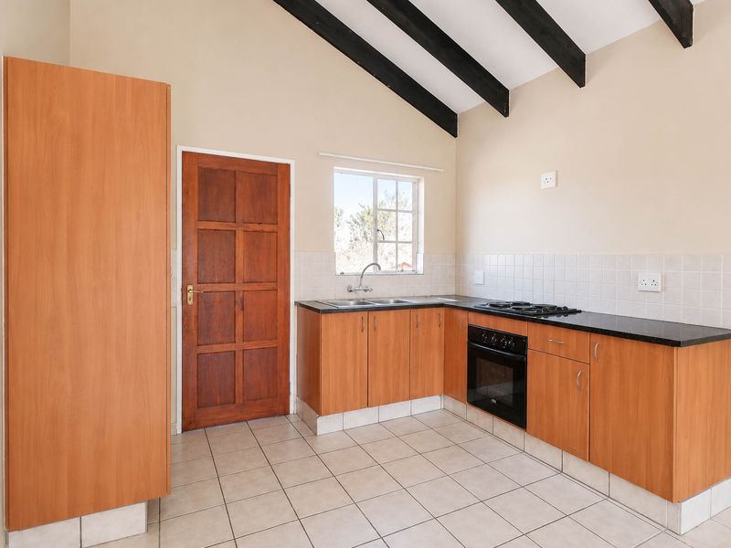 A functional kitchen featuring laminate cabinetry, granite countertops, built-in oven, gas hob, and exposed timber beams under a vaulted ceiling.