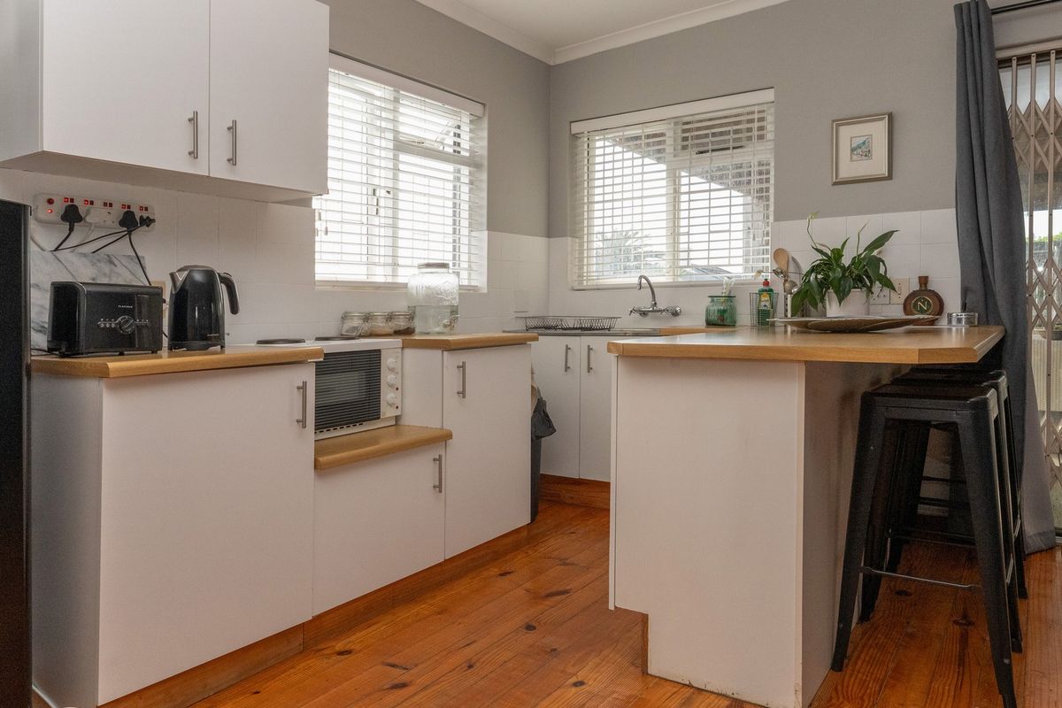 A functional kitchen featuring white cabinetry, wooden countertops, timber flooring, and a tiled splashback, offering a clean and practical workspace.