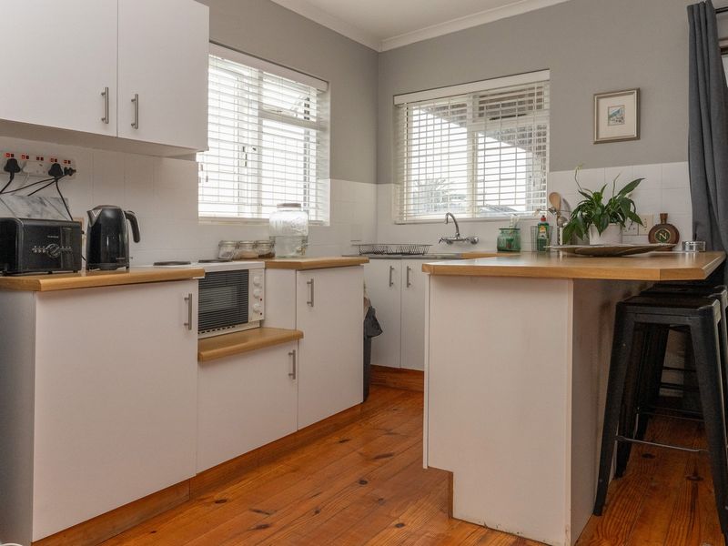 A functional kitchen featuring white cabinetry, wooden countertops, timber flooring, and a tiled splashback, offering a clean and practical workspace.