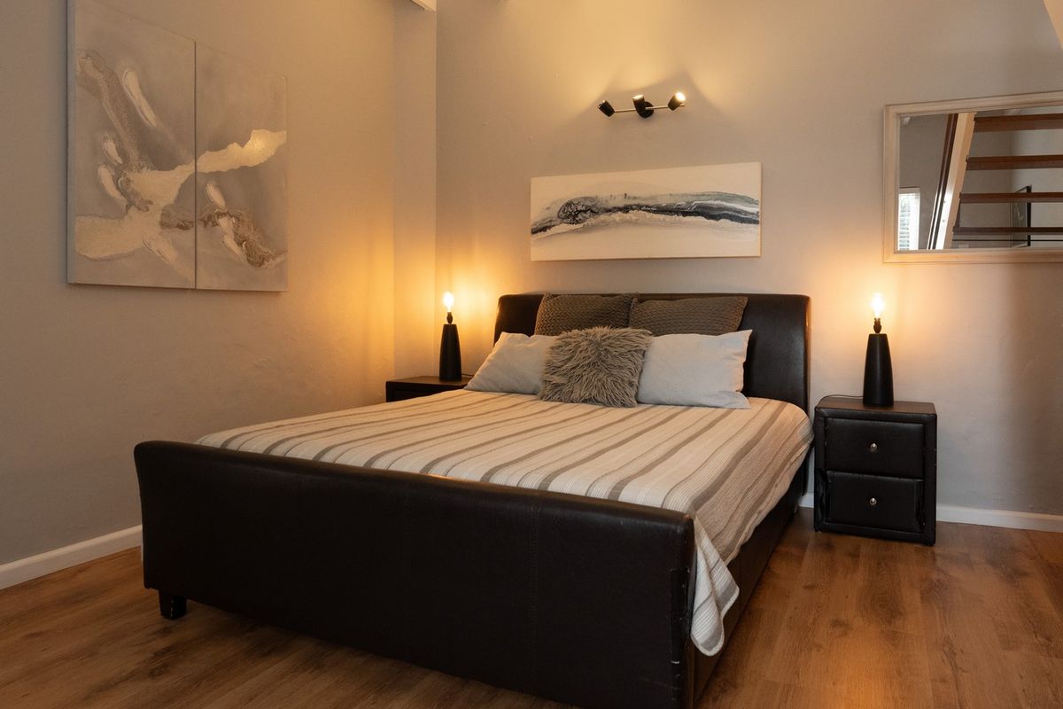 A well-maintained bedroom featuring laminate flooring, exposed ceiling beams, and warm accent lighting, creating a cozy and inviting atmosphere.