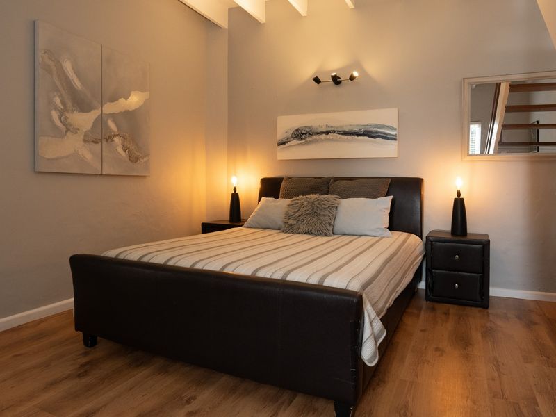 A well-maintained bedroom featuring laminate flooring, exposed ceiling beams, and warm accent lighting, creating a cozy and inviting atmosphere.