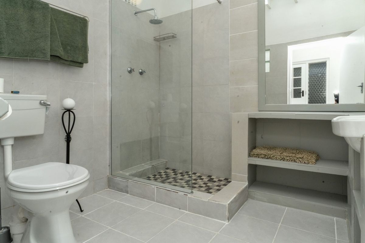 A modern bathroom featuring a walk-in shower with a glass screen, tiled walls and flooring, and a built-in vanity shelf with a mirror.