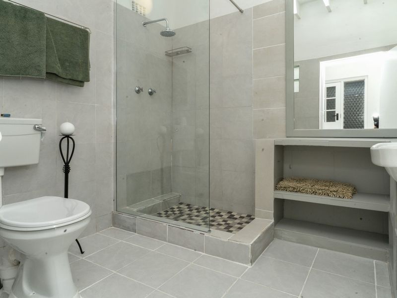 A modern bathroom featuring a walk-in shower with a glass screen, tiled walls and flooring, and a built-in vanity shelf with a mirror.