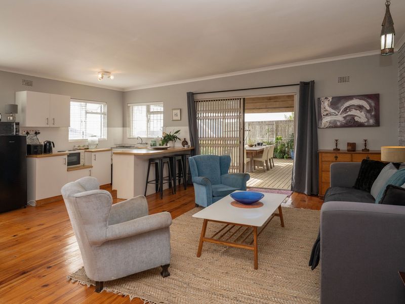 Spacious open-plan living area featuring warm timber flooring, a functional kitchen with island, and seamless flow to an outdoor patio through sliding doors.