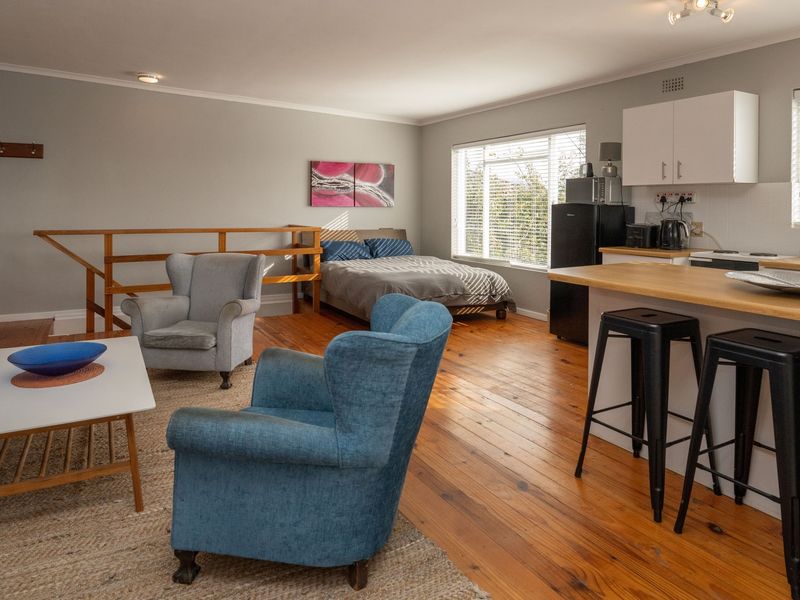 Open-plan living area featuring warm timber flooring, a functional kitchen with island seating, and a combined bedroom space with natural light.