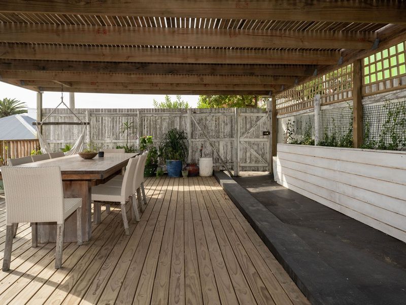 Covered outdoor patio featuring timber decking, a pergola structure, and built-in planter boxes, providing a functional space for outdoor dining and relaxation.