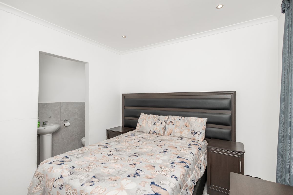 A well-maintained bedroom featuring recessed downlights and an adjoining en-suite area with a pedestal basin and tiled splashback.