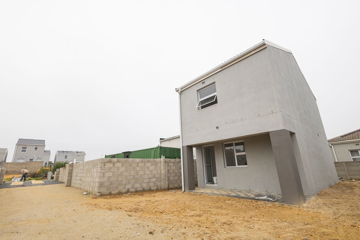 Rear view of a two-story townhouse featuring a plastered facade, paved patio area, and an unfinished surrounding garden space.
