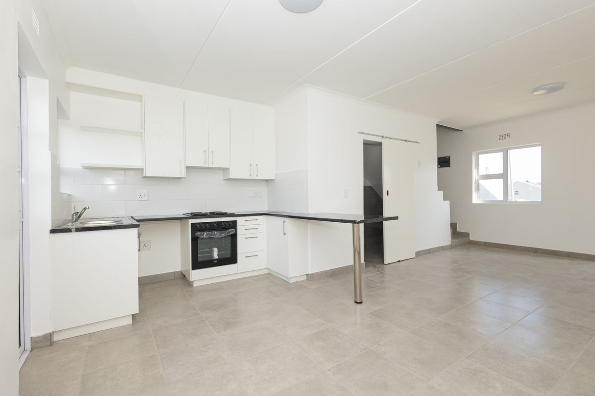 Open-plan kitchen and living area featuring white cabinetry, dark countertops, built-in oven, tiled flooring, and direct access to a staircase.