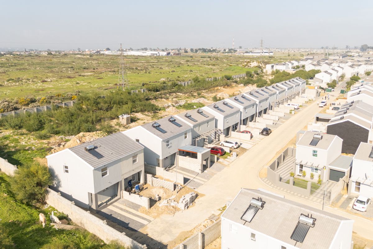 Aerial view of a townhouse development featuring multiple units with tiled roofs, solar geysers, and paved driveways in a suburban setting.