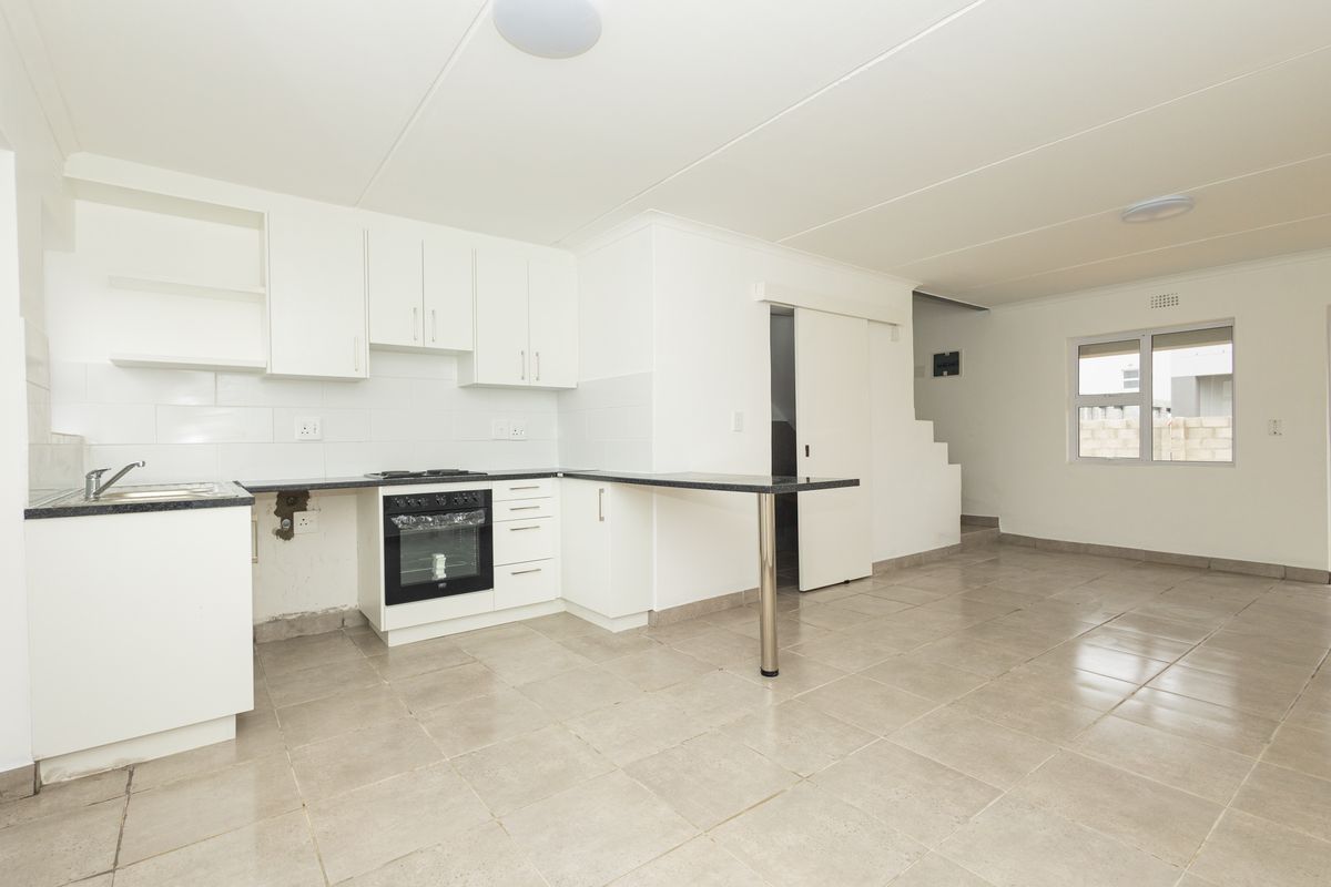 Open-plan kitchen and living area featuring white cabinetry, built-in oven, tiled flooring, and direct access to a staircase.