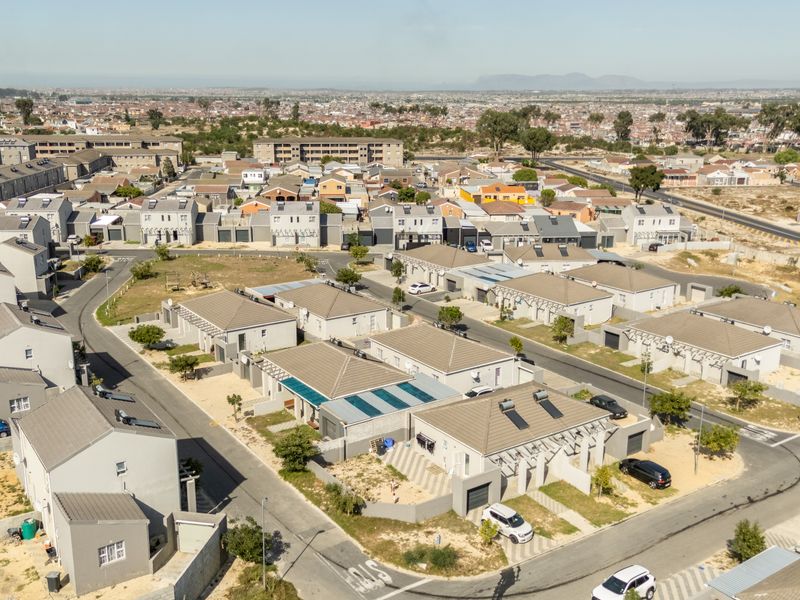 Aerial view of a residential townhouse estate featuring multiple units with tiled roofs, solar water heating systems, and paved driveways.