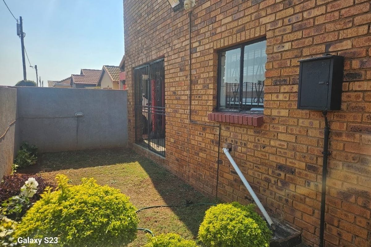 Rear exterior view of the property featuring face brick walls, security gates, and a small garden area.