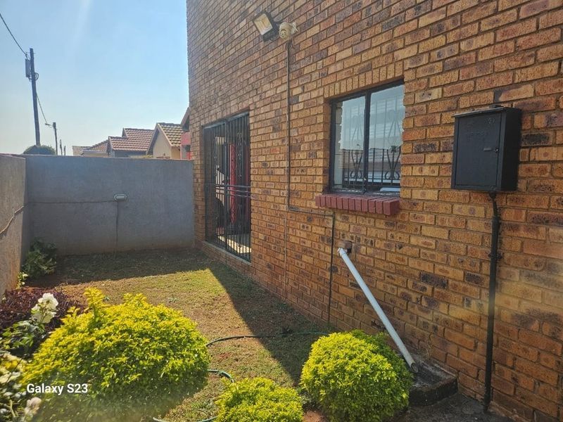 Rear exterior view of the property featuring face brick walls, security gates, and a small garden area.
