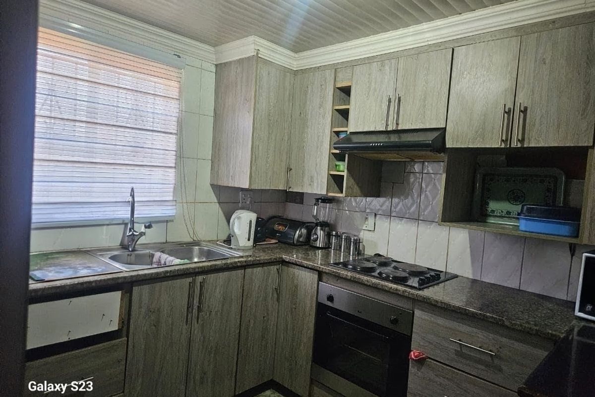 Functional kitchen featuring wood-look cabinetry, granite countertops, built-in oven, and hob, with a tiled backsplash and window blinds.