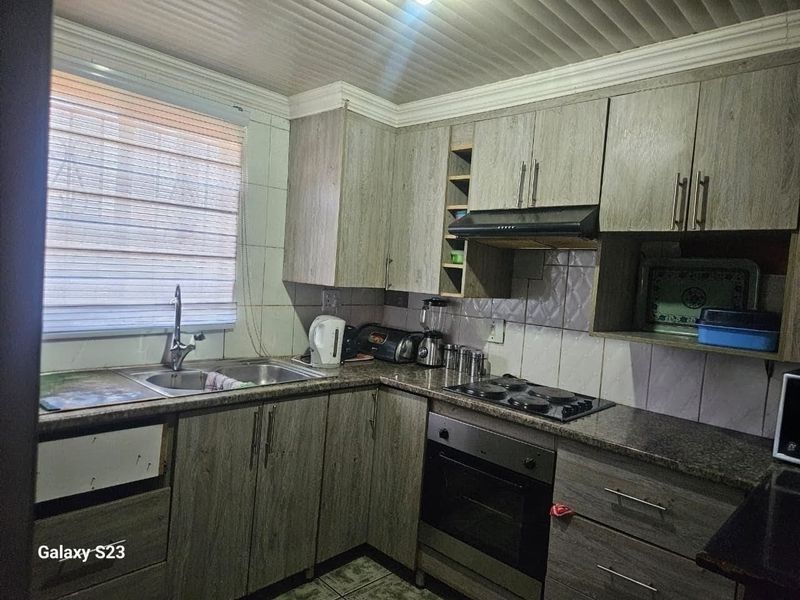 Functional kitchen featuring wood-look cabinetry, granite countertops, built-in oven, and hob, with a tiled backsplash and window blinds.